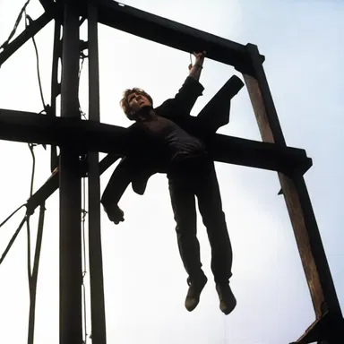 The suspenseful movie scene showed the protagonist desperately reaching for a clamp to hold a falling structure in place.