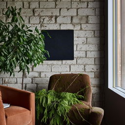 Architectural photography of a textured brick wall with a stylish armchair, a pot of sprawling green branches, and a large black and white abstract artwork