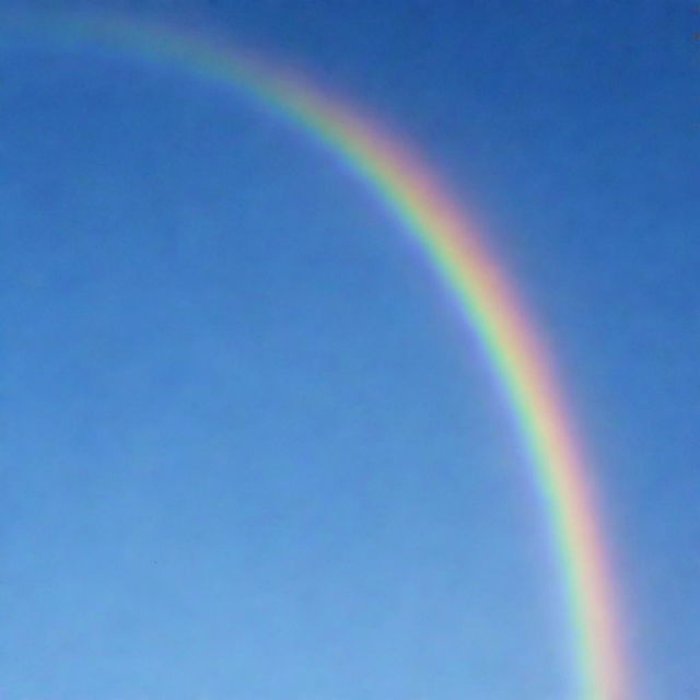 A vibrant, multi-colored rainbow arc stretching across a clear blue sky.