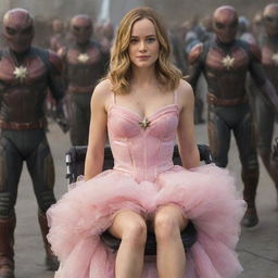 Captain Marvel's Brie Larson adorned in a pink dress, sitting in a baby stroller being pushed by friendly aliens.