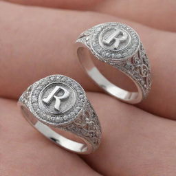 Two similar silver engagement rings. The first one, feminine style, with the letter R intricately crafted on it. The second one, masculine style, with the letter J elegantly etched onto it.