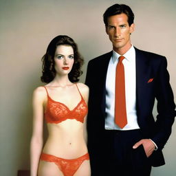 A slender, white man with an effeminate form, wearing a small red lace bra and panties, standing next to his wife who is dressed in a suit and tie