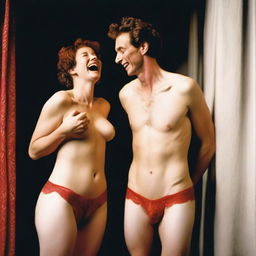 A slender, white man with an effeminate form, wearing a small red lace bra and panties, standing next to his wife who is laughing at him