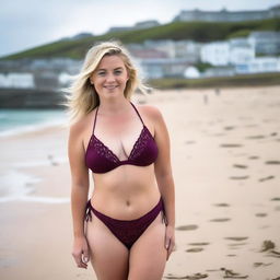 A curvy and voluptuous blonde woman with her hair tied back is posing on St Ives beach with the town behind her