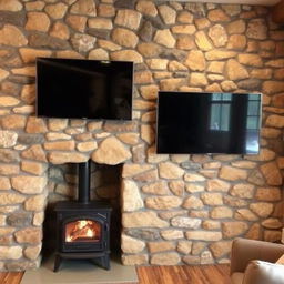 A cozy living room with a rustic design, featuring a stone accent wall that complements a wood-burning stove and a mounted television