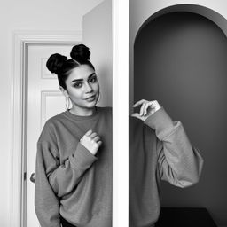 A confident woman posing in front of a mirror, wearing a casual gray sweatshirt, her hair styled in two buns