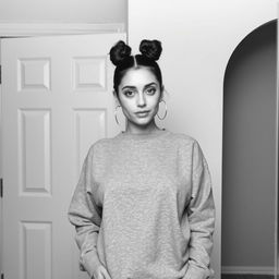 A confident woman posing in front of a mirror, wearing a casual gray sweatshirt, her hair styled in two buns