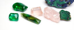 A stunning arrangement of crystals on a pristine white background, featuring emerald, rose quartz, green aventurine, lapis lazuli, and malachite