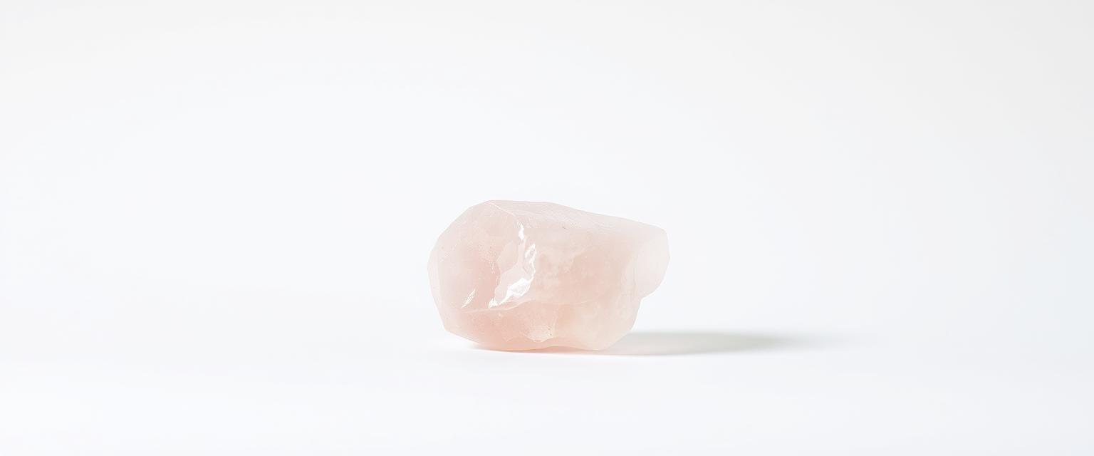 A single piece of rose quartz crystal displayed on a stark white background