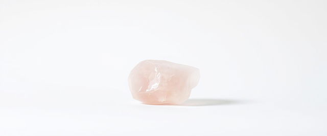 A single piece of rose quartz crystal displayed on a stark white background