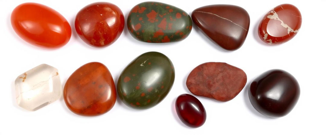 A collection of carnelian, bloodstone, red jasper, clear quartz, and garnet on a white background