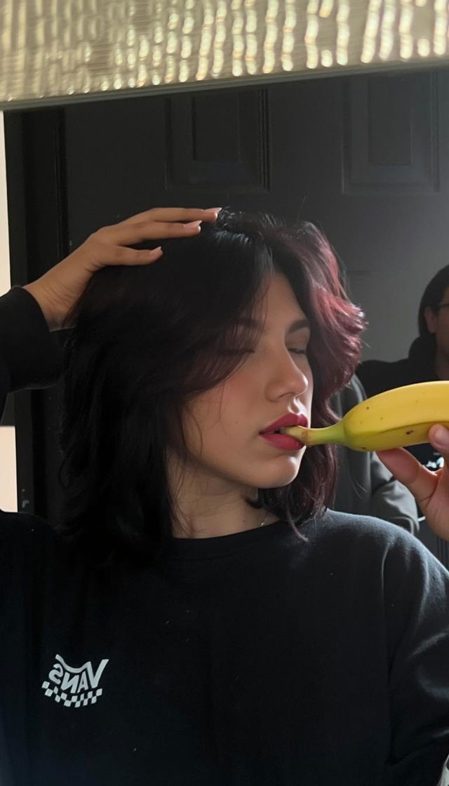 A person wearing a black Vans shirt is holding a banana close to their face