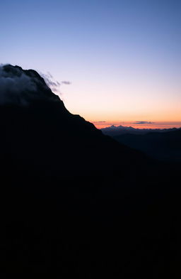 A majestic black mountain rising against a twilight sky, partially shrouded in mist