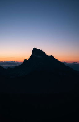 A majestic black mountain rising against a twilight sky, partially shrouded in mist