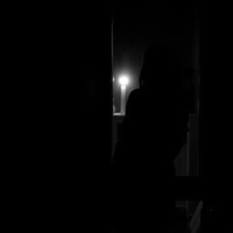 a woman approaching a window and gazing outside at night, captured in a dark, black and white image