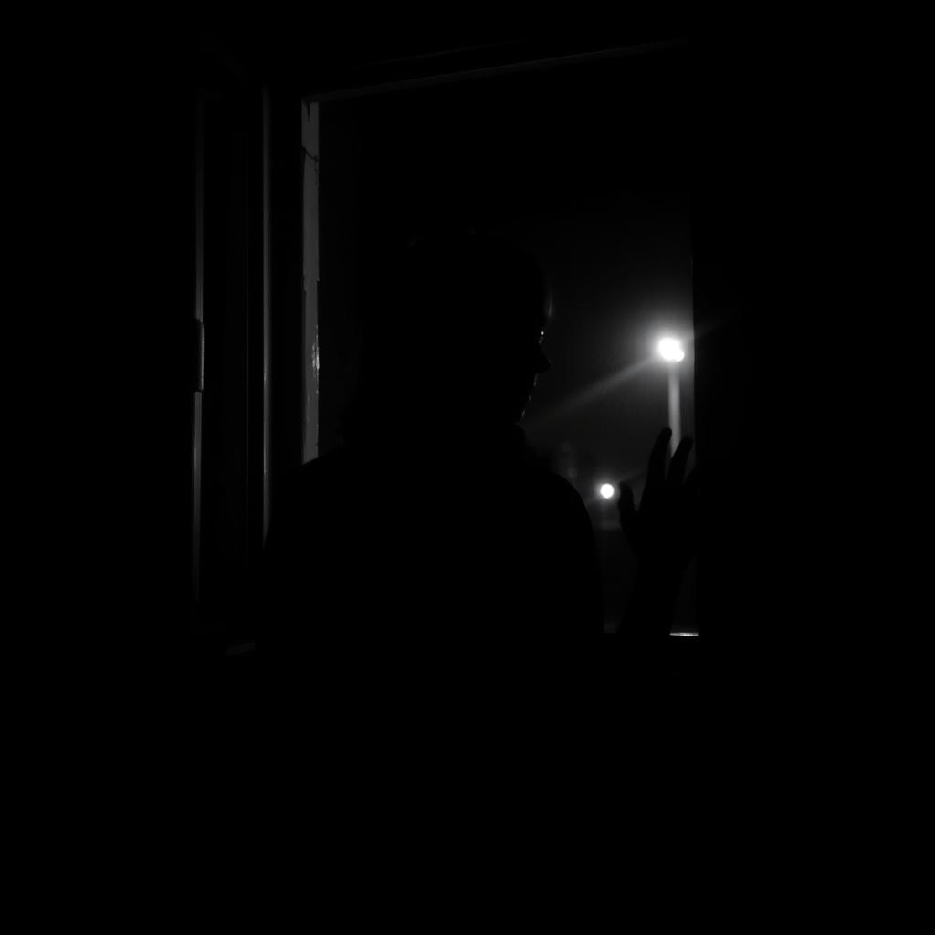 a woman approaching a window and gazing outside at night, captured in a dark, black and white image