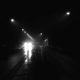 a dark and empty street, depicting rain falling illuminated by street lights, captured in a moody black and white image