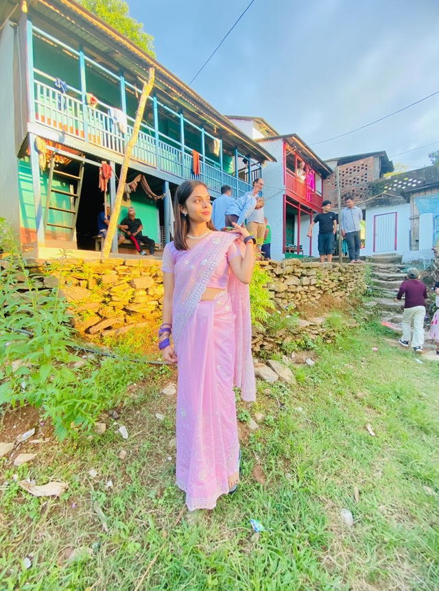 A beautiful woman in a traditional lavender sari standing in front of colorful traditional houses in a picturesque village