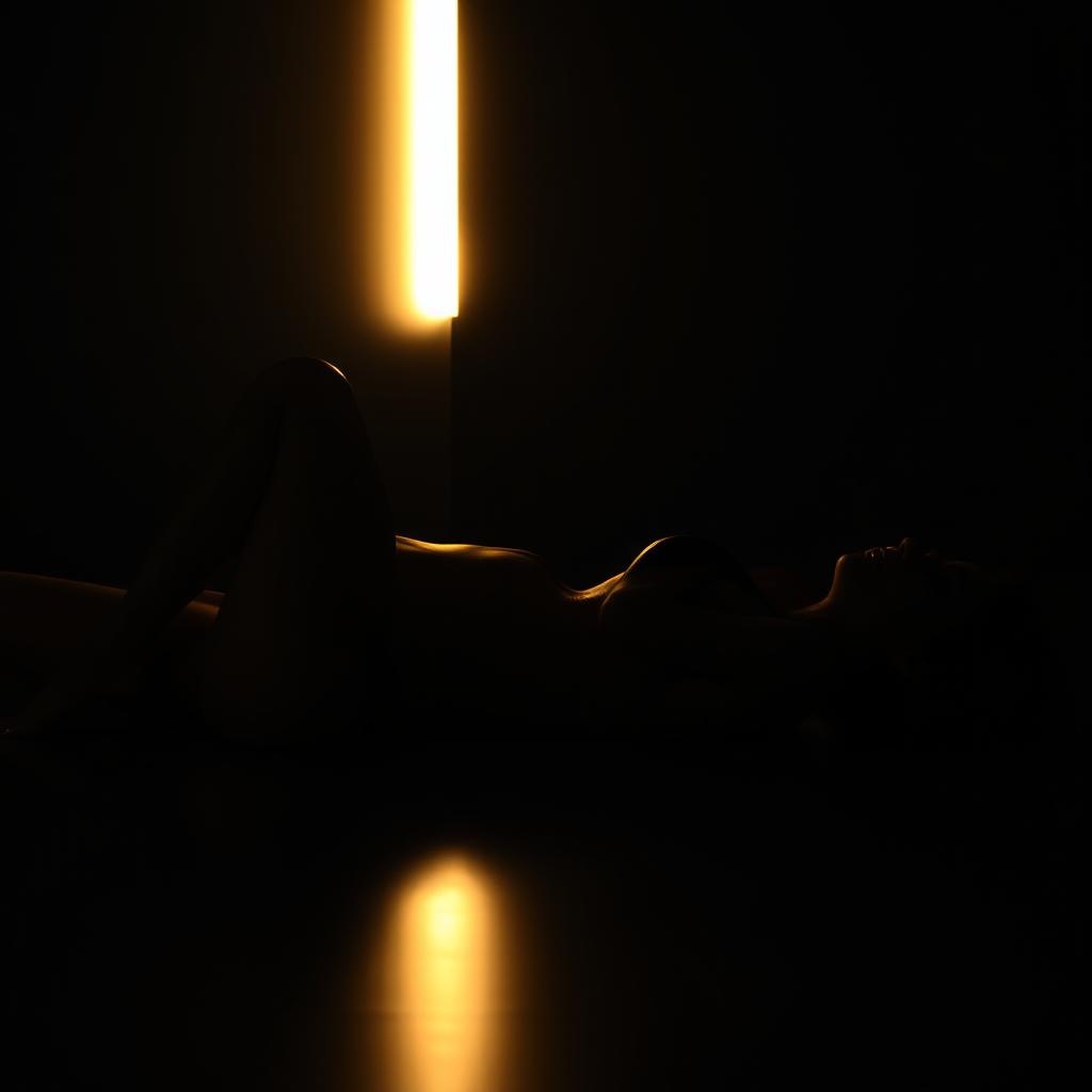 An artistic and realistic photo capturing the illuminated silhouette of a young, slender woman in a swimsuit, lying on her back in a completely dark space