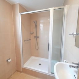 a bathroom with a shower tray and shower set on the right side, a sink on the right side, beige tiled walls, no toilet