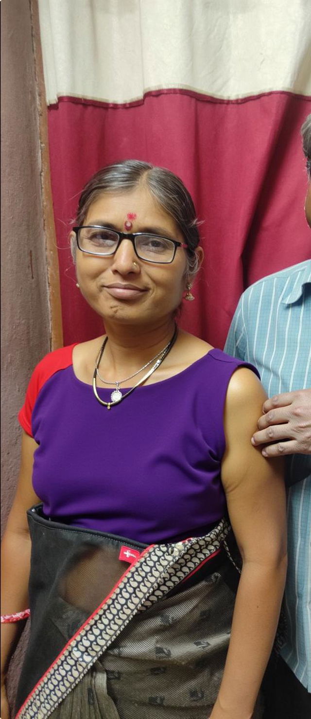 A woman wearing a stylish violet blouse paired with a black and patterned sari, standing indoors with a neutral expression