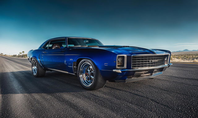 Daytime low angle side shot of a beefed-up 1969 Chevrolet Camaro on an open highway.