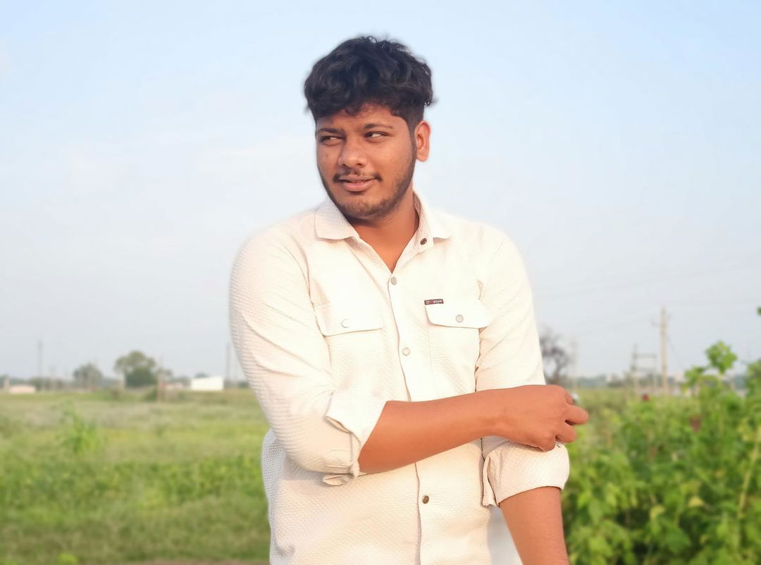 An appealing young man with a charming smile, casually dressed in a light-colored shirt with the sleeves rolled up, standing against a picturesque rural backdrop