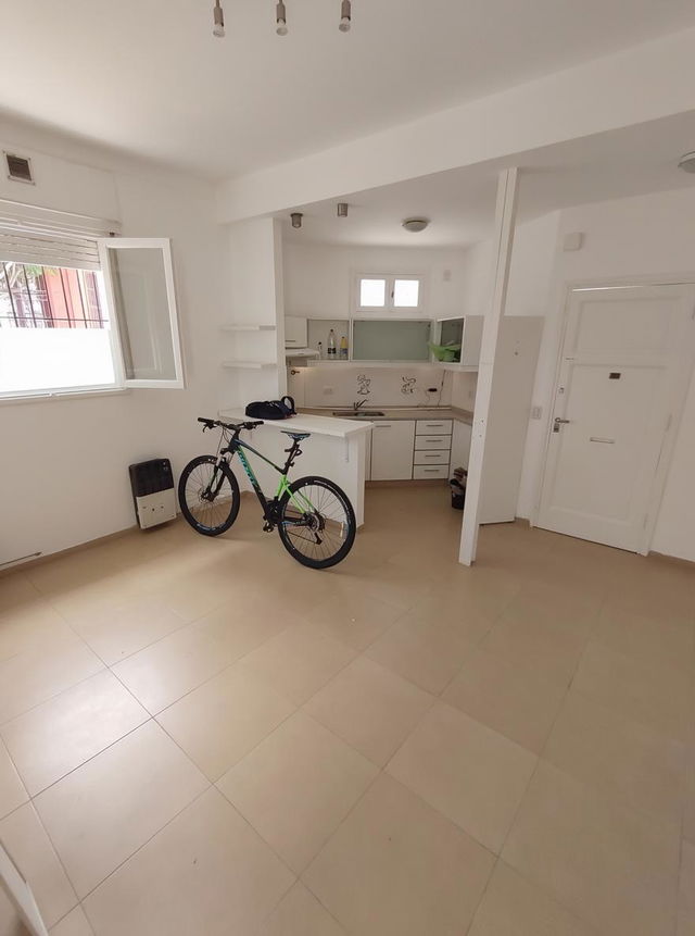 A modern, minimalistic interior of a small kitchen and living area, featuring light beige tiled flooring