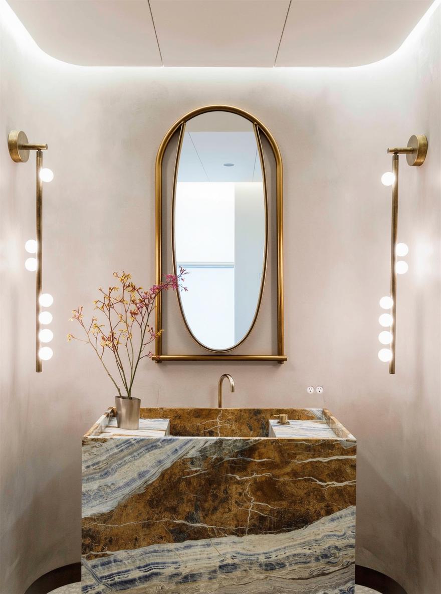 A sophisticated bathroom featuring a large, modern mirror that dominates the space above a luxurious stone sink with captivating brown and gold veining