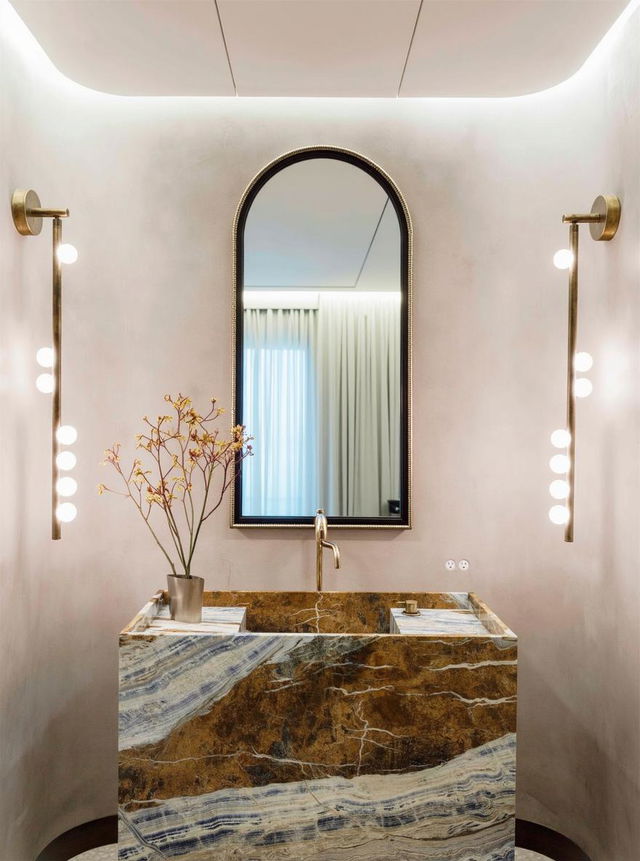 A stylish bathroom design featuring a large, modern oval mirror with a sleek gold frame, perfectly positioned above an elegant stone sink with stunning blue and gold marbling