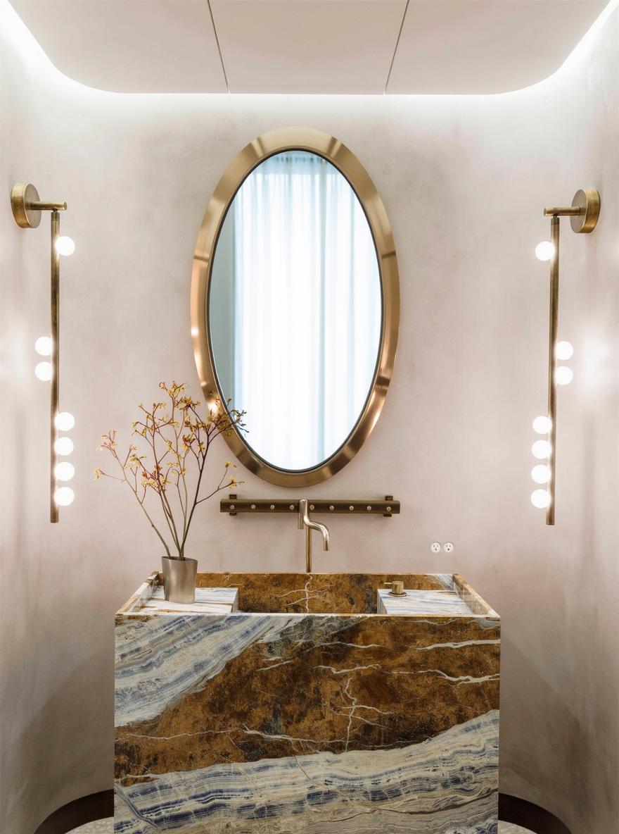 A sleek, modern bathroom featuring an impressive large oval mirror with a thin gold frame, reflecting the stylish interior design