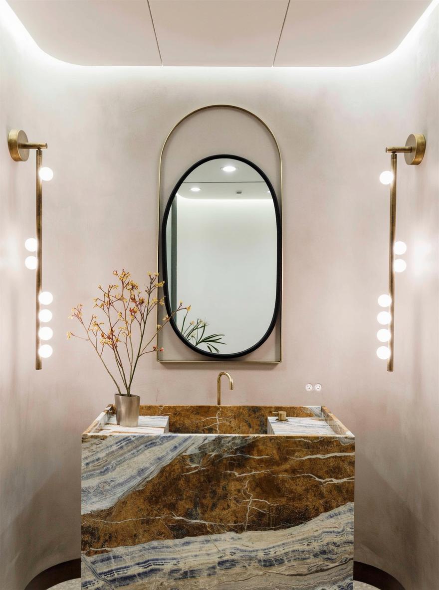 A stylish bathroom featuring a large modern oval mirror that elegantly hangs above a striking marble sink with beautiful brown and blue veining