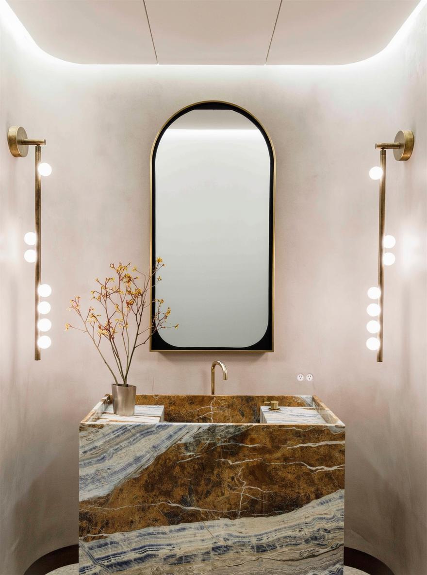 A contemporary bathroom featuring a large modern mirror with a sleek oval shape, positioned over a luxurious, beautifully veined marble sink in shades of brown and blue