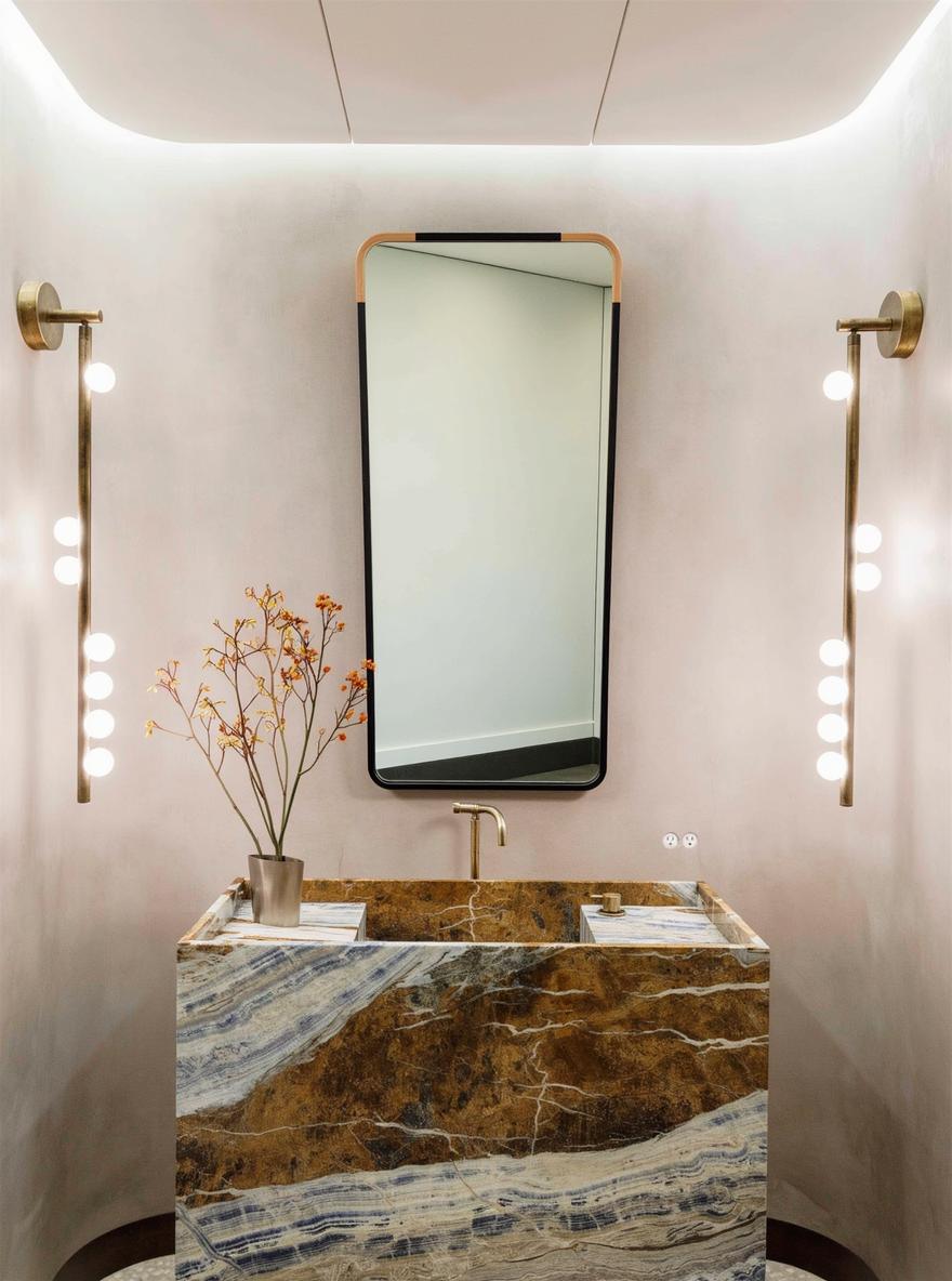 An upscale bathroom featuring a large, modern oval mirror above an elegant marble sink with striking brown and gold veining