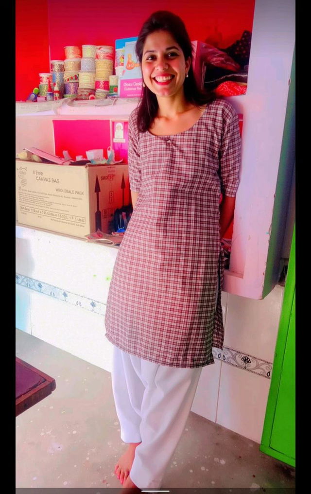 A young woman standing gracefully in a colorful room, wearing a stylish checked kurta paired with white loose-fitting trousers