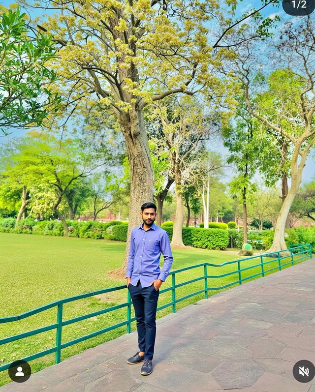 A young man standing confidently in a picturesque park filled with vibrant green trees and lush grass