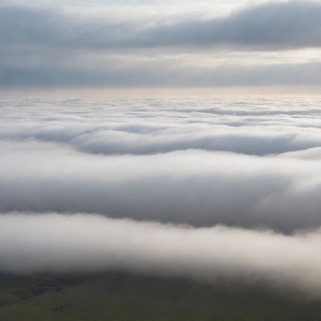 A vast, sprawling landscape disappearing into a misty horizon under a sky filled with soft, billowing clouds.