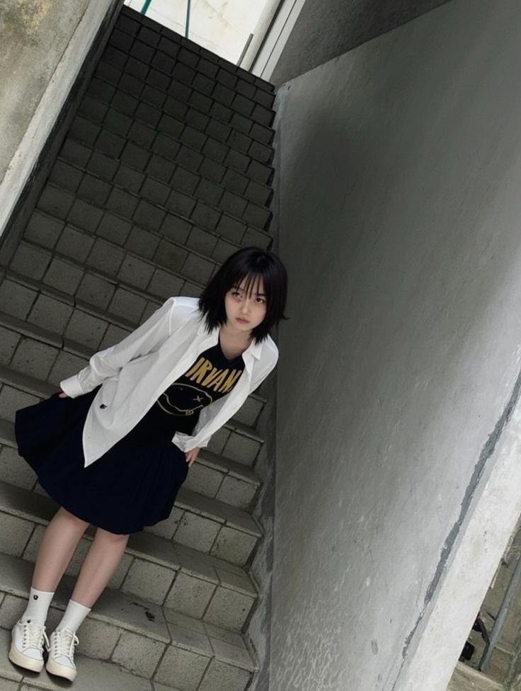 A moody and atmospheric scene featuring a young woman with straight black hair standing on a staircase in an urban setting