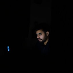 A man seated in a dark room in Iran, intently looking at a computer screen