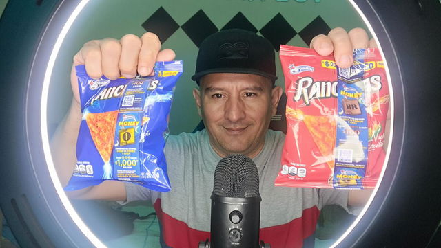 A close-up ASMR scene featuring a man holding two bags of snacks, one blue labeled 'Panticos' and one red labeled 'Ranchitas'