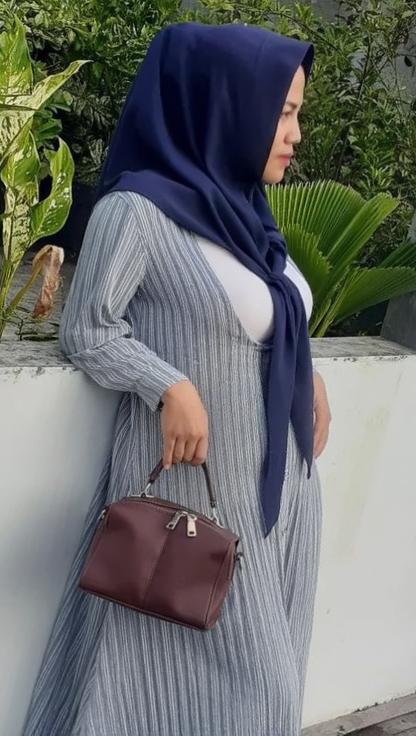 A stylish woman wearing an elegant striped dress with long sleeves, complemented by a navy blue hijab that frames her face beautifully