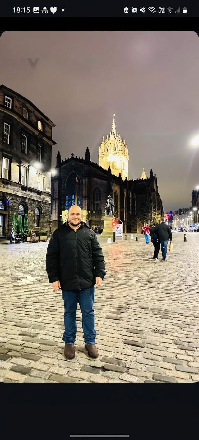 A nighttime street scene with cobblestone pavement, illuminated historical buildings on either side, a tall gothic church in the background lit by warm light, creating a magical atmosphere