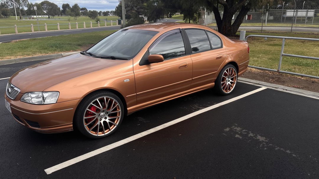 A sleek, metallic orange car parked in a modern setting, showcasing 19-inch white Ford Mustang tyres and rims