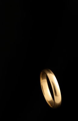 A simple gold ring positioned sideways against a mysterious black background, creating a striking contrast
