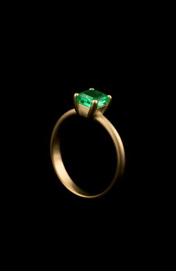 A simple golden ring with an emerald stone, positioned sideways, set against a mysterious black background