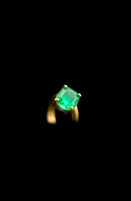 A simple golden ring with an emerald stone, positioned sideways, set against a mysterious black background