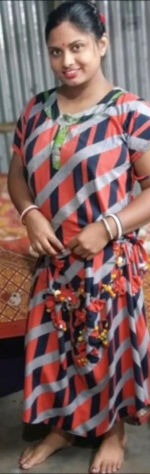 A young woman standing confidently, wearing a colorful and patterned traditional dress with shades of red, blue, and grey