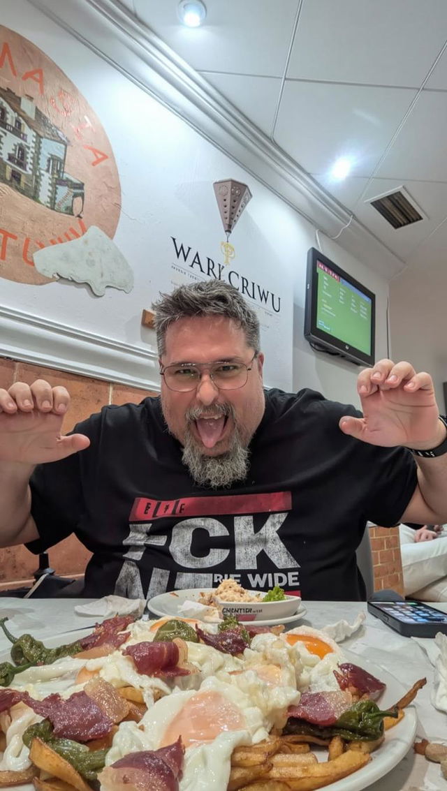 A humorous and vibrant film poster featuring a cheerful bearded man with glasses, excitedly posing with a giant plate of nachos topped with runny eggs, crispy bacon, and green peppers