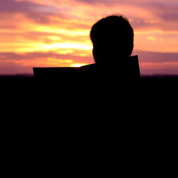 A silhouette of a person standing against a stunning sunset, holding an open book