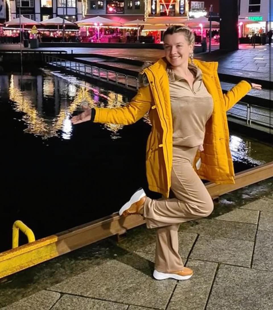 A confident woman posing joyfully by a scenic waterfront at night